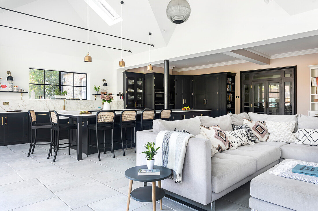 Open-plan kitchen with black cupboards, dining area and light-coloured couch in the adjoining living area