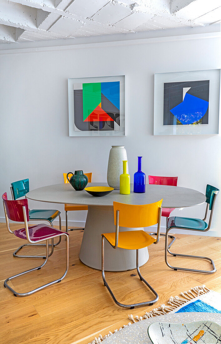 Oval dining table with colorful chairs, modern art on the wall