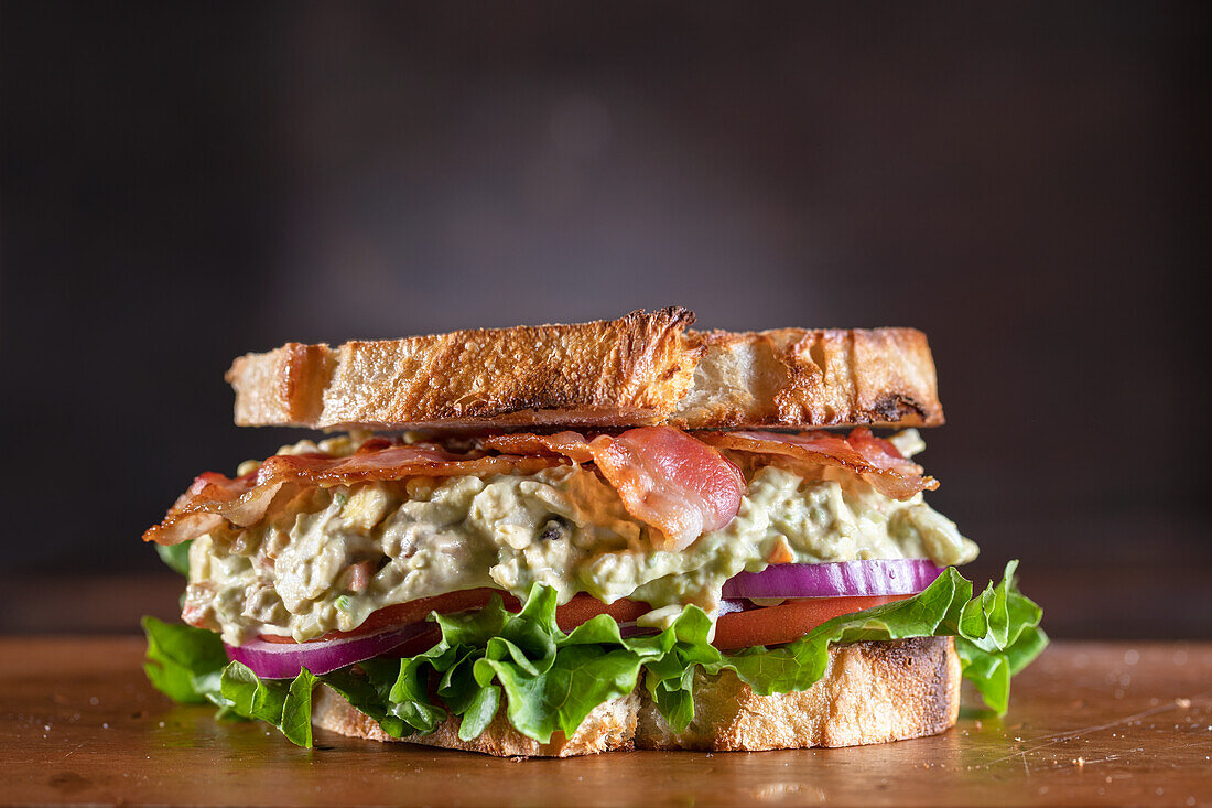 Avocado and egg salad sandwich with bacon, lettuce, tomatoes and red onions