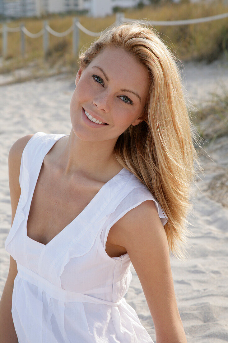 Blonde woman in white summer dress on the beach