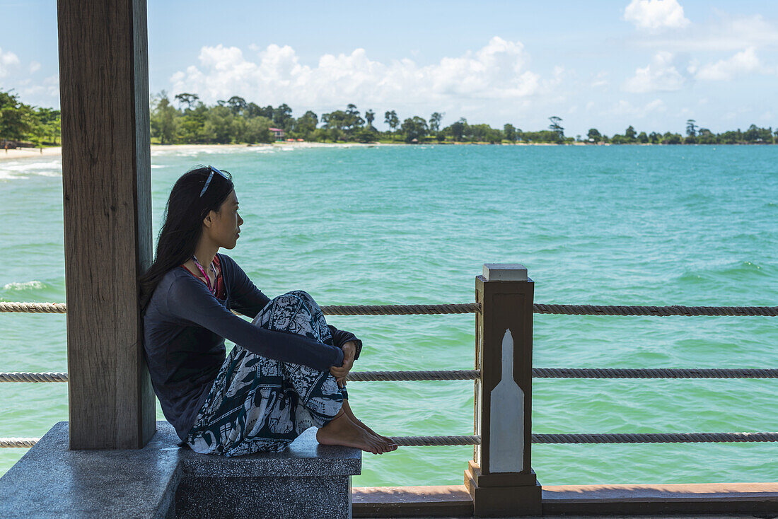 A Young Woman Sits On The Pier At Independence Beach; Sihanoukville, Cambodia