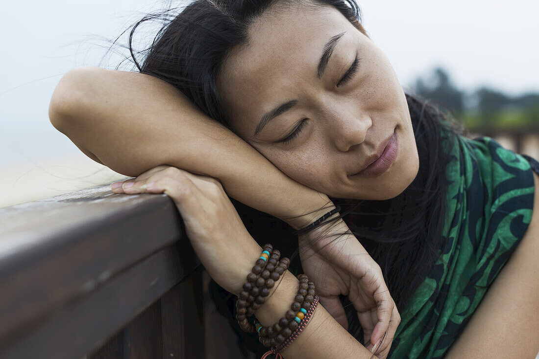 Eine junge Frau legt ihren Kopf gegen ein hölzernes Geländer am Strand; Jincheng, Kinmen, Taiwan