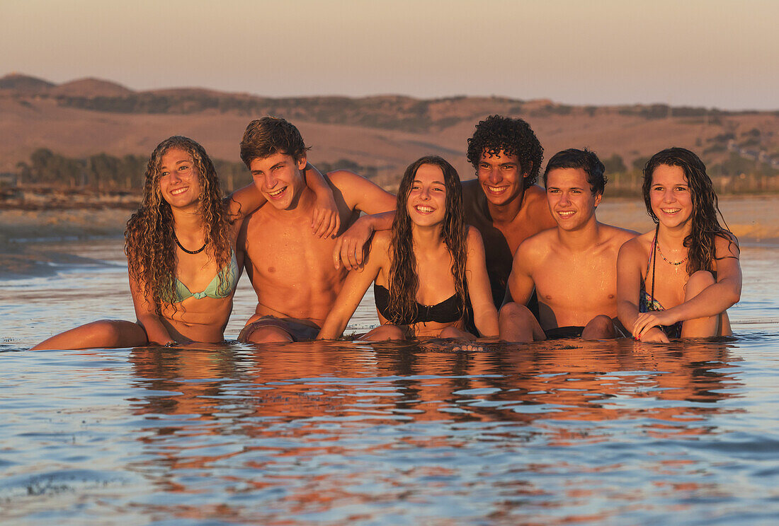 A group of teenagers in bathing suits sitting in water at sunset; Tarifa,  Cadiz, Andalusia, Spain - Stock Photo - Dissolve