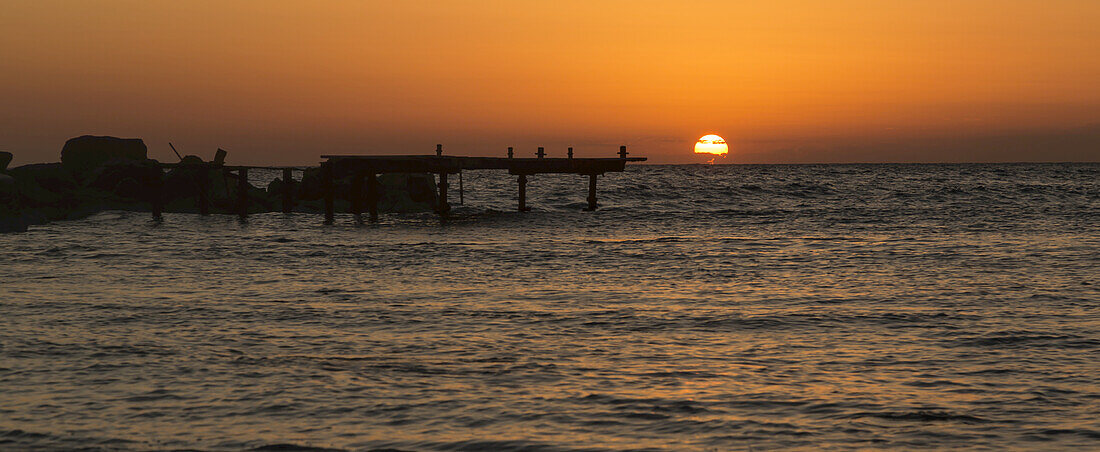 Die goldene Sonne versinkt hinter dem Wasser bei Sonnenuntergang mit orangefarbenem Himmel; Paphos, Zypern