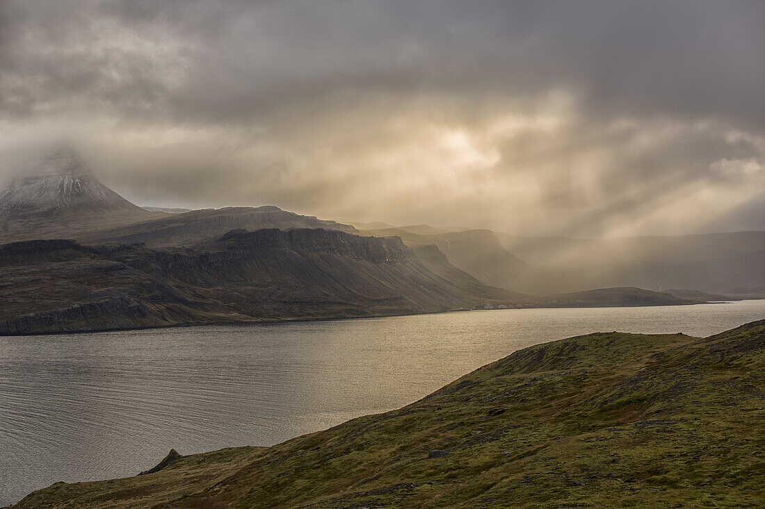 Lichtstrahlen leuchten auf die Berge und das verlassene Dorf Djupavik; Island