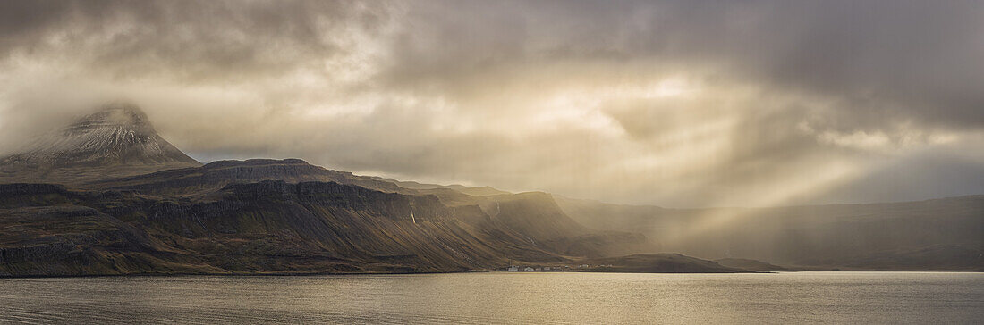 Die Sonne scheint durch die Sturmwolken und erzeugt schöne Sonnenstrahlen in der Nähe des verlassenen Dorfes Djupavik; Island