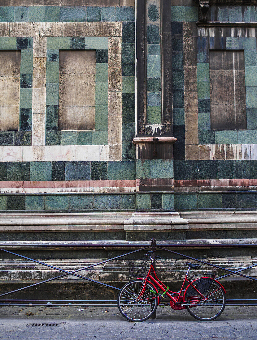 Ein rotes Fahrrad kontrastiert mit dem grünen Granit des Gebäudes dahinter; Florenz, Italien