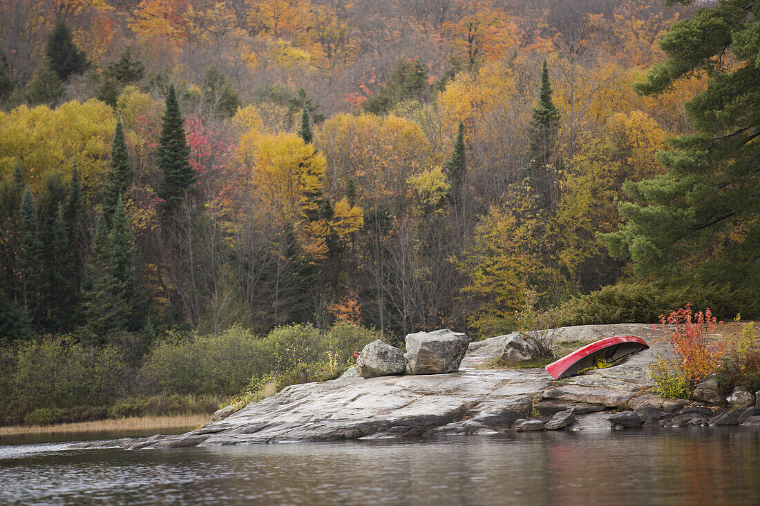 Red Canoe Sitting On The Rocks Surrounding Rock Lake, Algonquin Park; Ontario, Canada