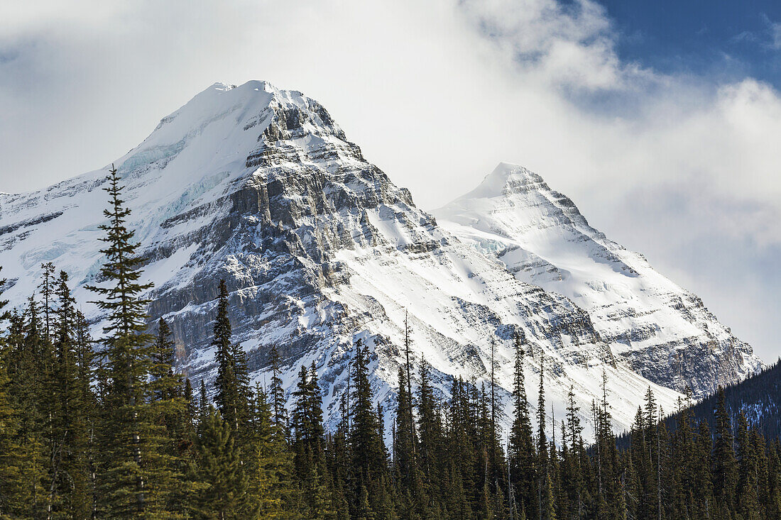 Nahaufnahme von zwei schneebedeckten Berggipfeln mit Wolkendecke und etwas blauem Himmel; Banff, Alberta, Kanada