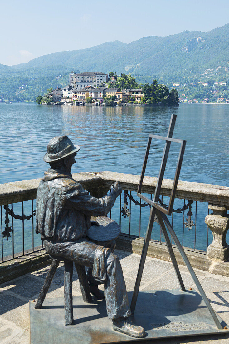 Statue eines Künstlers, der an einer Staffelei sitzt und malt, mit Blick auf die Insel San Giulio am Orta-See; Orta, Piemont, Italien