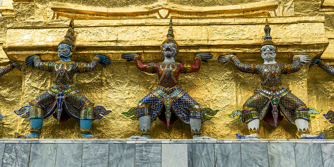 Three Statues Along A Gold Wall, Temple Of The Emerald Buddha (Wat Phra Kaew); Bangkok, Thailand