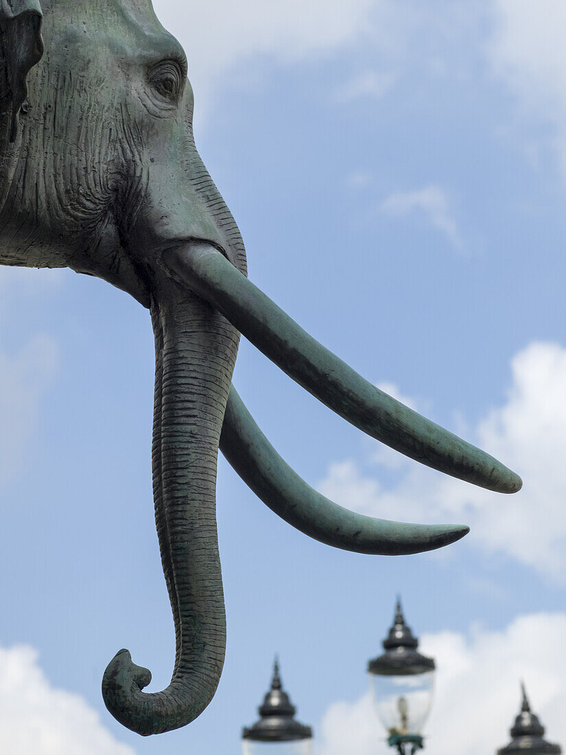 Skulptur eines Elefanten mit Stoßzähnen und Laternenpfählen im Hintergrund; Bangkok, Thailand