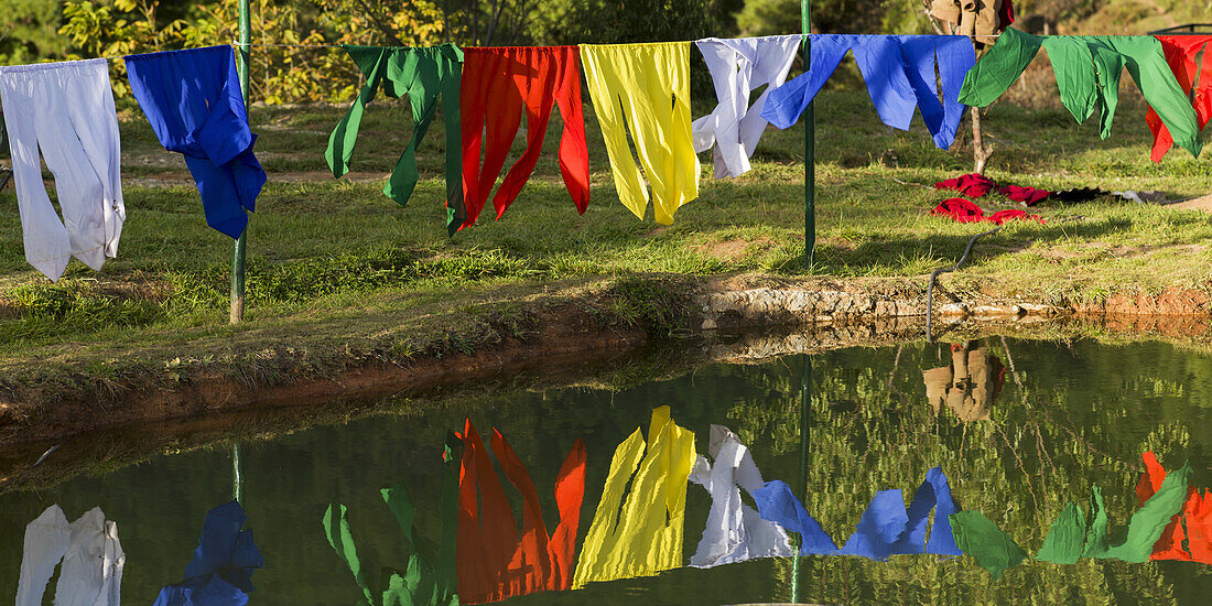 Bunte Gebetsfahnen, die im Wasser hängen und sich darin spiegeln; Paro, Bhutan