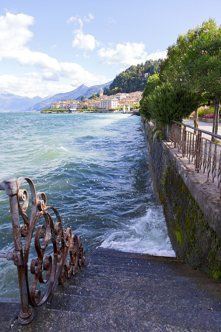 Der Wind lässt das Wasser des Comer Sees gegen eine Ufertreppe und einen Bürgersteig plätschern; Bellagio, Italien