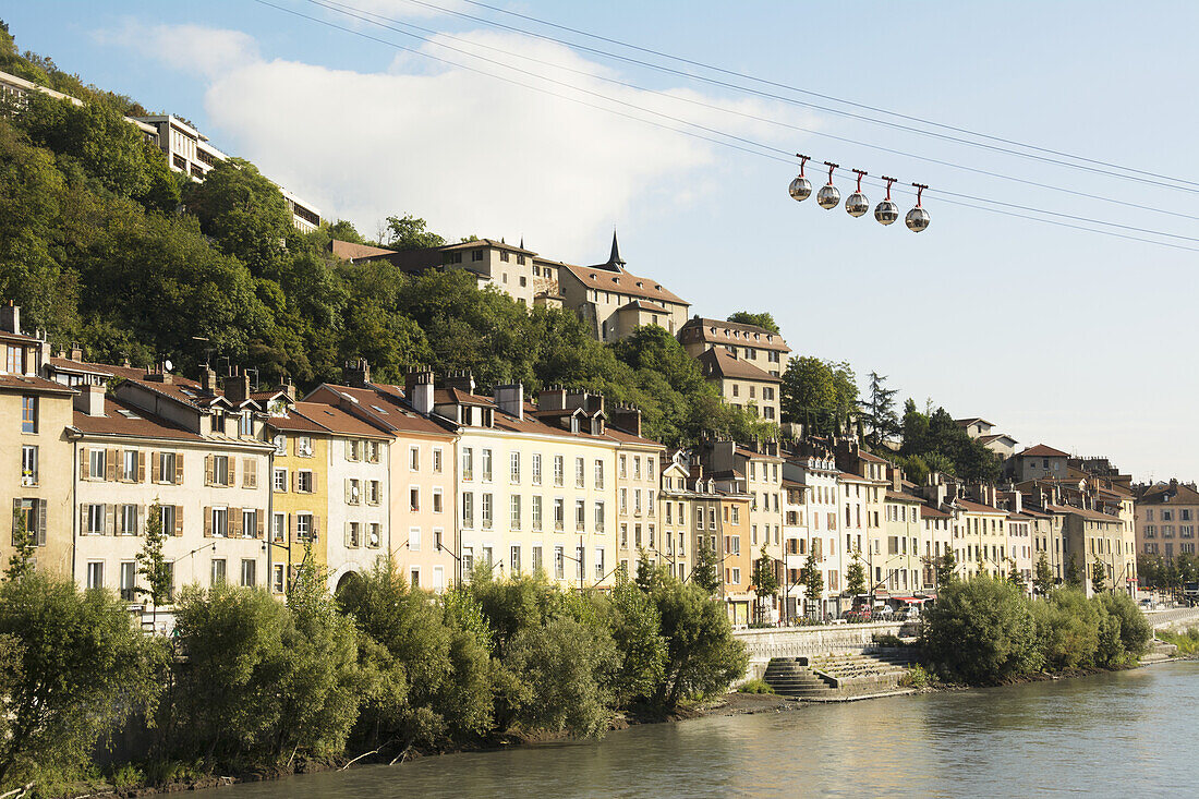 Bubble Gondola Passing Over Old Buildings Along A River; Grenoble, France