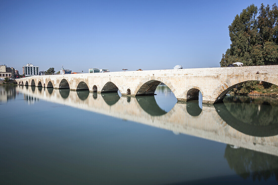Antike römische Brücke, die sich im ruhigen Wasser des Seyhan-Flusses spiegelt; Adana, Türkei