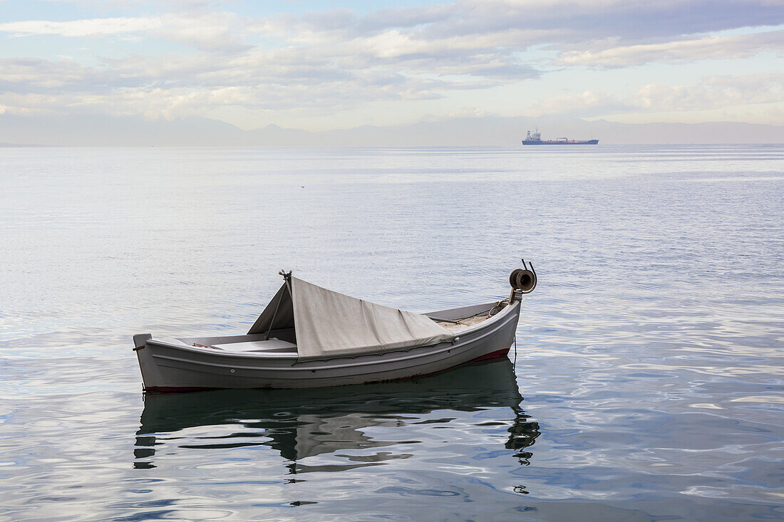 Ein Boot schwimmt auf der ruhigen Ägäis mit einem Schiff in der Ferne; Thessaloniki, Griechenland