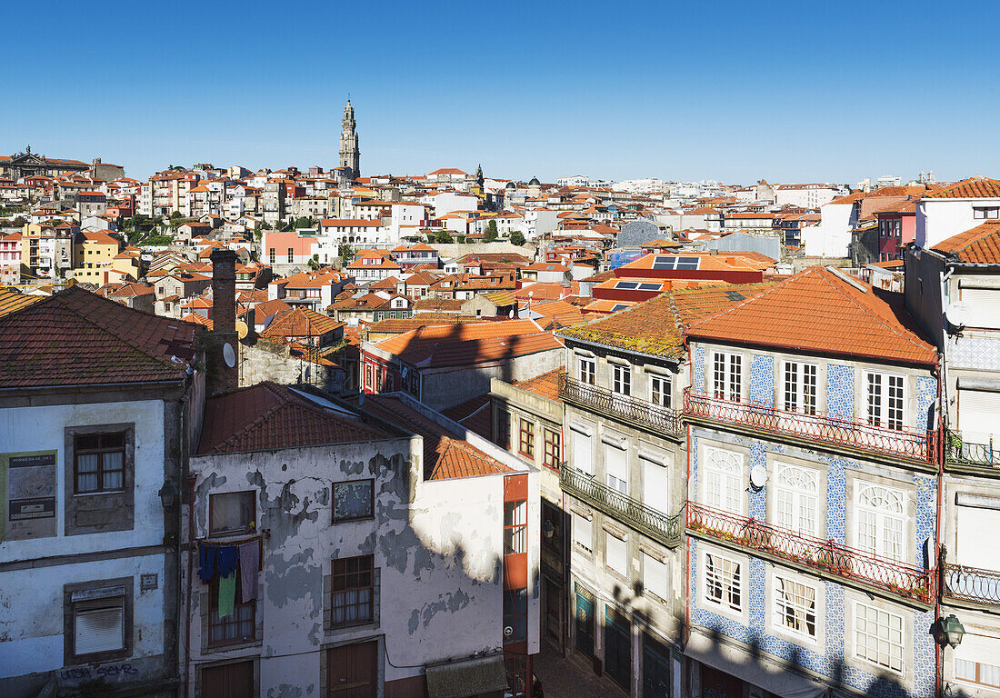 Dächer von Häusern und ein Turm in der Ferne vor blauem Himmel; Porto, Portugal