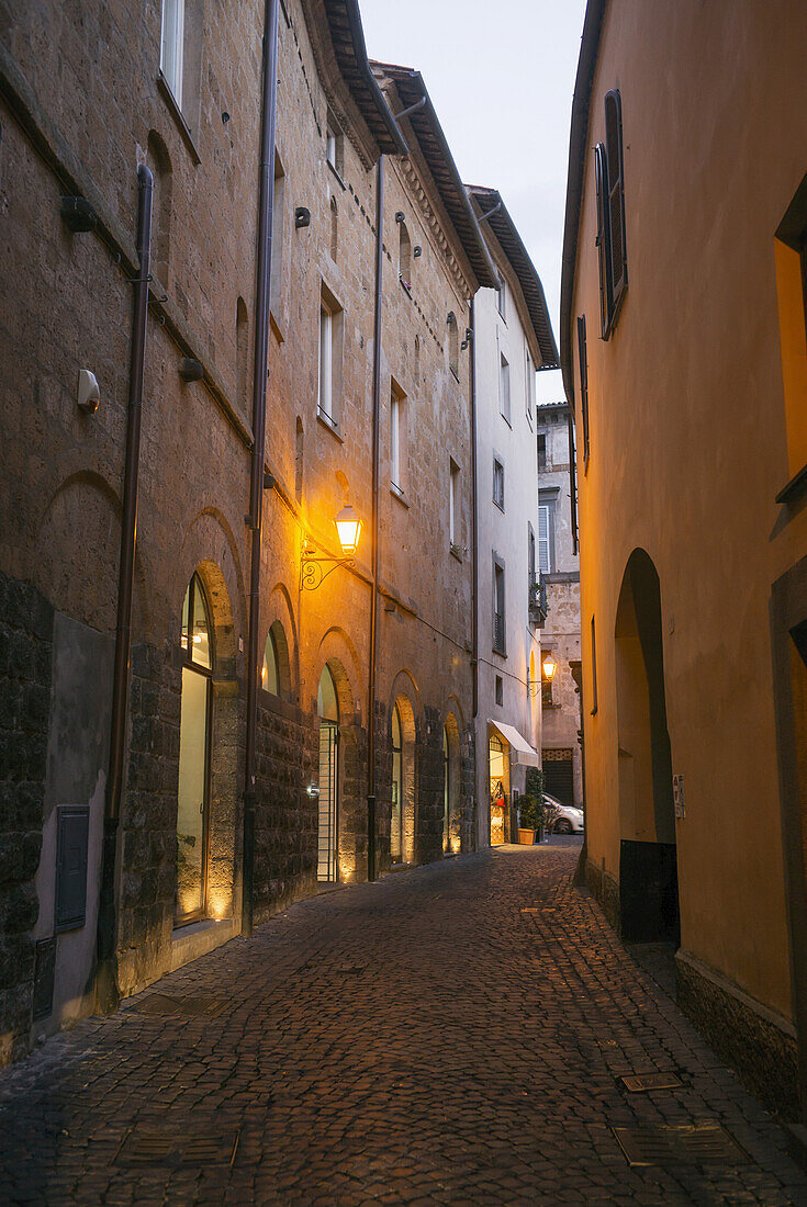 A Narrow Street Between Buildings With A Golden Light Illuminated At Dusk; Orvieto, Umbria, Italy