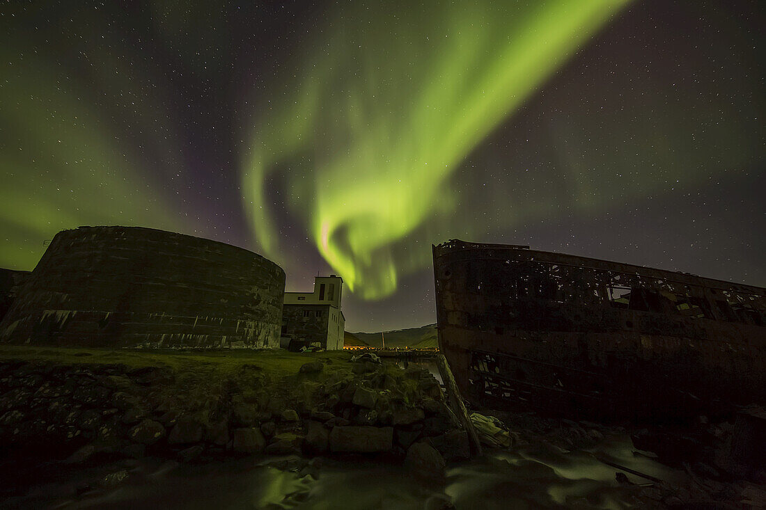 Nordlichter über der Stadt Djupavik entlang der Strandir-Küste, hier tanzen sie über der alten Heringsfabrik und dem Schiffswrack; Djupavik, Island