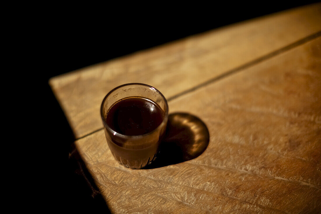 Ein Glas heißer Kaffee steht im Sonnenlicht, hergestellt aus gerösteten und mit einem hölzernen Mörser gemahlenen Bohnen, keine 200 Meter entfernt. Muara Pinang ist ein riesiges Kaffee produzierendes Dorf; Sumatra, Indonesien