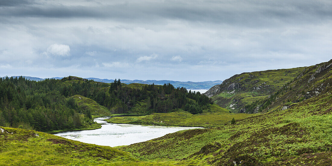 A River Flowing Into A Pond Surrounded By Lush Grass And Forest In The Highlands; Scotland