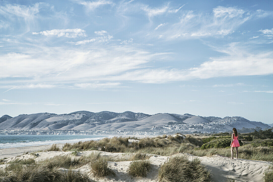 Frau steht auf einer Sanddüne mit Blick auf den Ozean; San Luis Obispo, Kalifornien, Vereinigte Staaten von Amerika