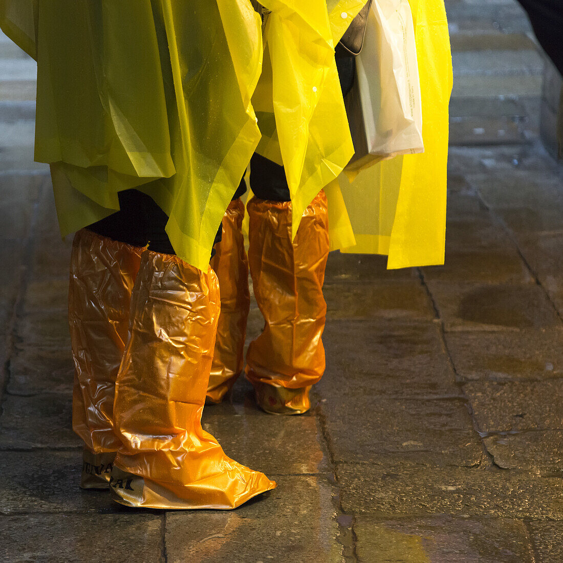People Standing With Yellow Rain Ponchos And Footwear Covered In Orange Plastic Covers; Venice, Italy