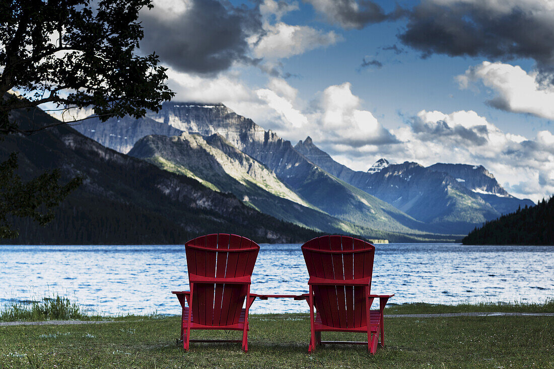 Zwei rote Adirondack-Stühle sitzen mit Blick auf den See und die Rocky Mountains, Waterton Lakes National Park; Alberta, Kanada