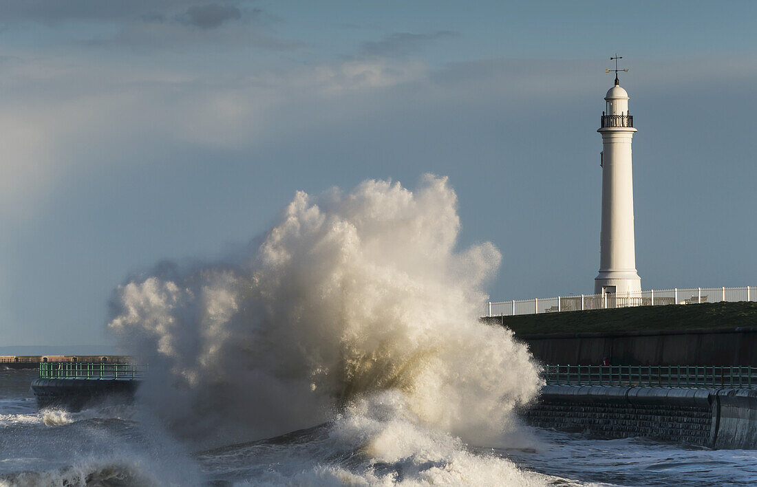 Eine große Welle bricht und kracht gegen das Ufer vor einem Leuchtturm; Sunderland, Tyne And Wear, England