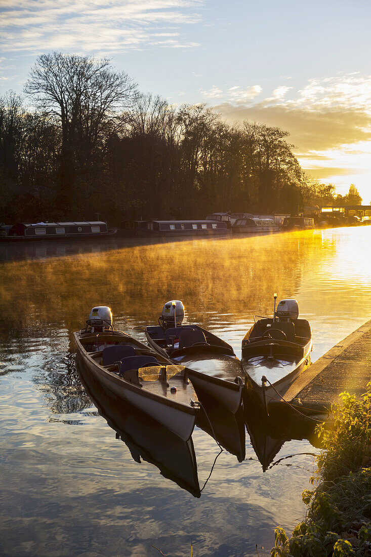 Sonnenaufgang über dem Fluss Molesey und kleine Motorboote, die am Ufer vertäut sind; Surrey, England