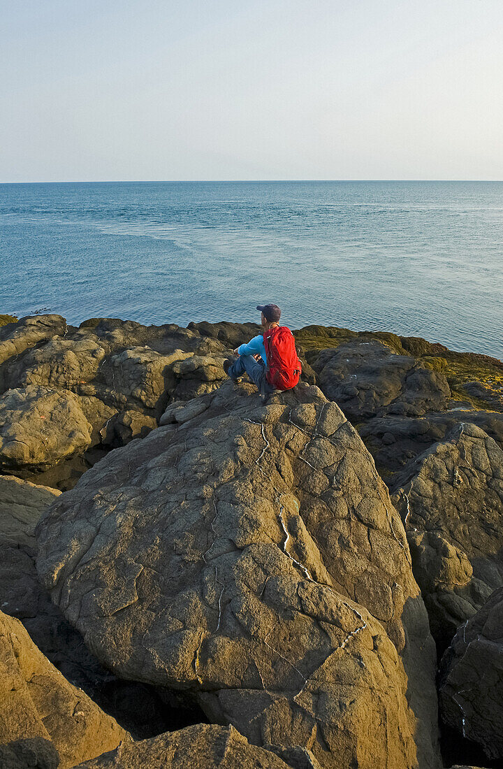 Hiker Sits On A Rock With A View Of The Shoreline, Bay Of Fundy; Long Island, Nova Scotia, Canada