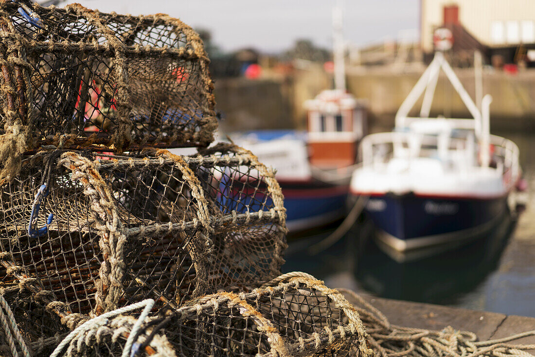 Traps Sitting On The Shore With Fishing Boats Moored In The Background; St. Abbs Head, Scottish Borders, Scotland