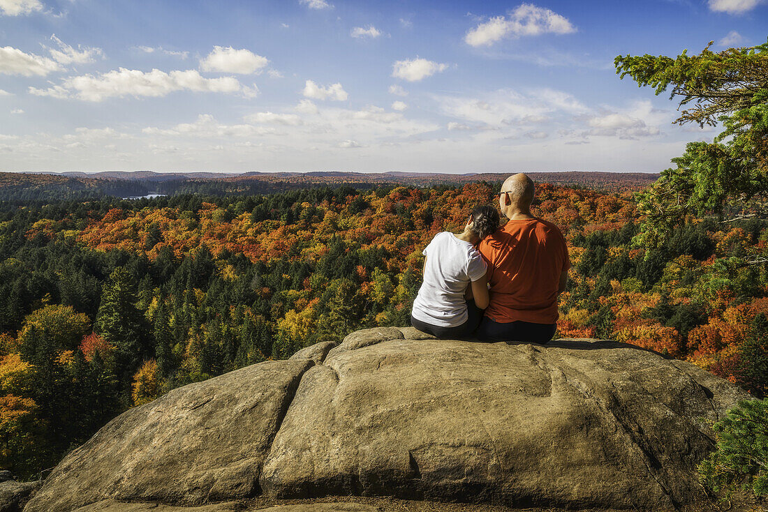 Paar sitzt auf einer Klippe mit Blick auf die Herbstfarben im Algonquin Park, Frau hat Kopf auf der Schulter des Mannes; Ontario, Kanada
