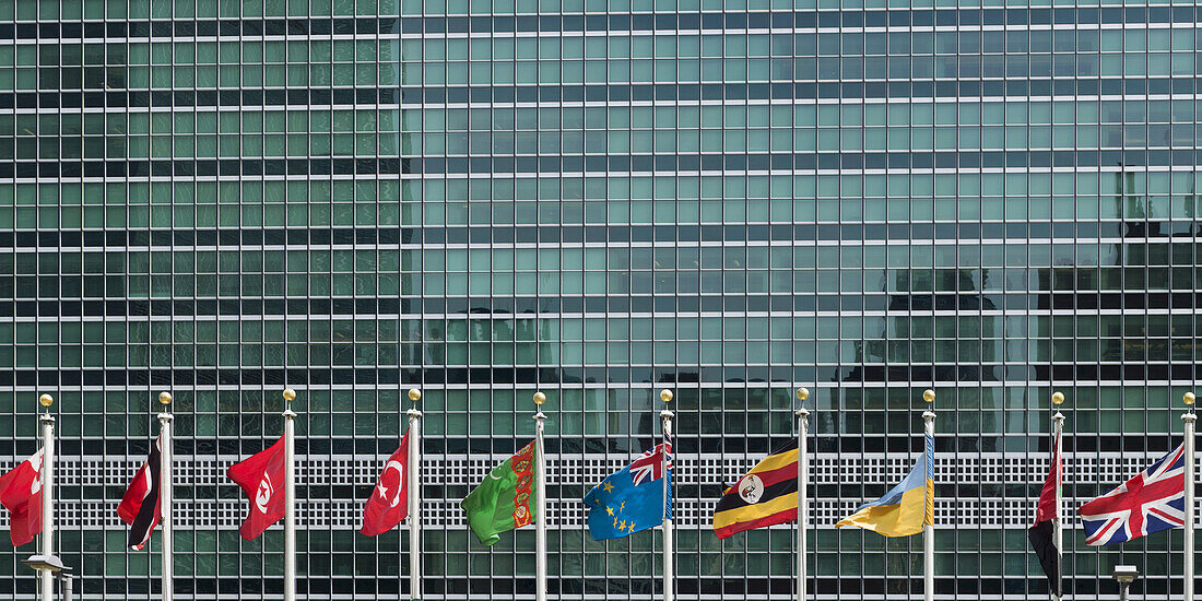 International Flags In A Row In Front Of A Headquarters Of The United Nations Building With Glass Facade; New York City, New York, United States Of America
