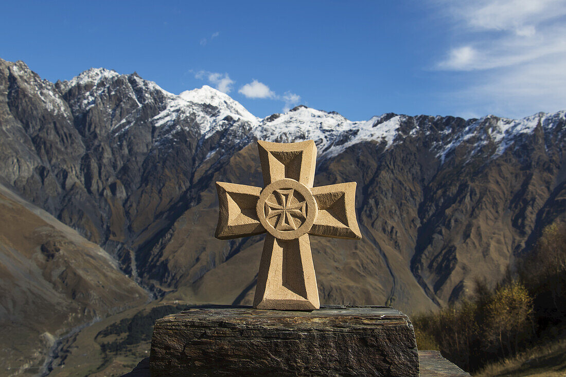 Stone Fountain With A Cross With The Caucasus Mountains In The Background; Kazbegi, Mtskheta-Mtianeti, Georgia