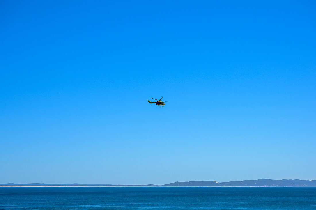 Helicopter in a blue sky over the ocean along the coast of Australia; Noosa Heads, Queensland, Australia