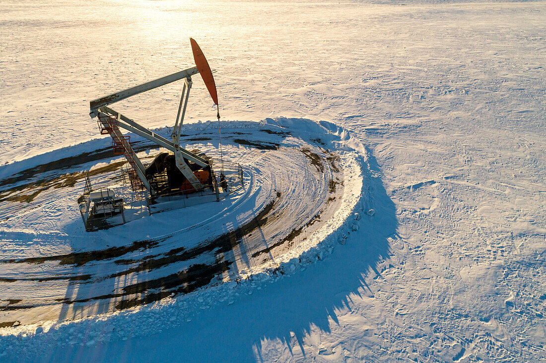 Aerial view of pumpjack in snow-covered field at sunrise; Longview, Alberta, Canada