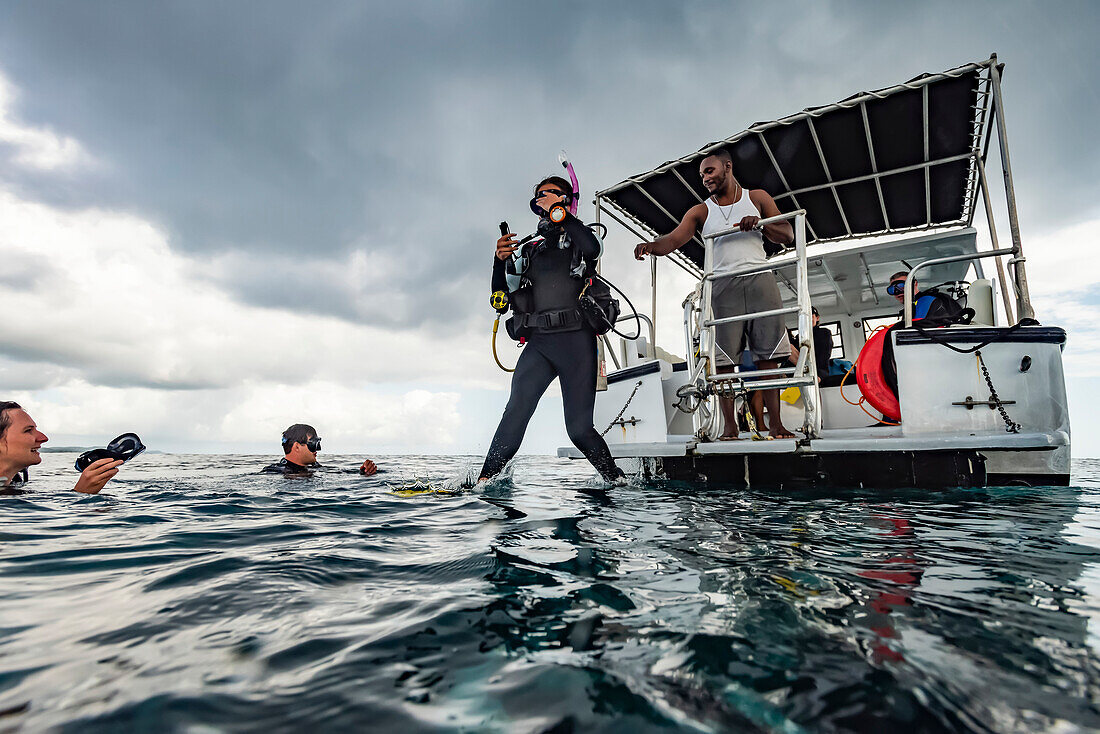 Scuba divers enter the water from a boat for their tour of the Cemetery Wall dive site on the South side of Roatan Island; Roatan, Bay Islands Department, Honduras