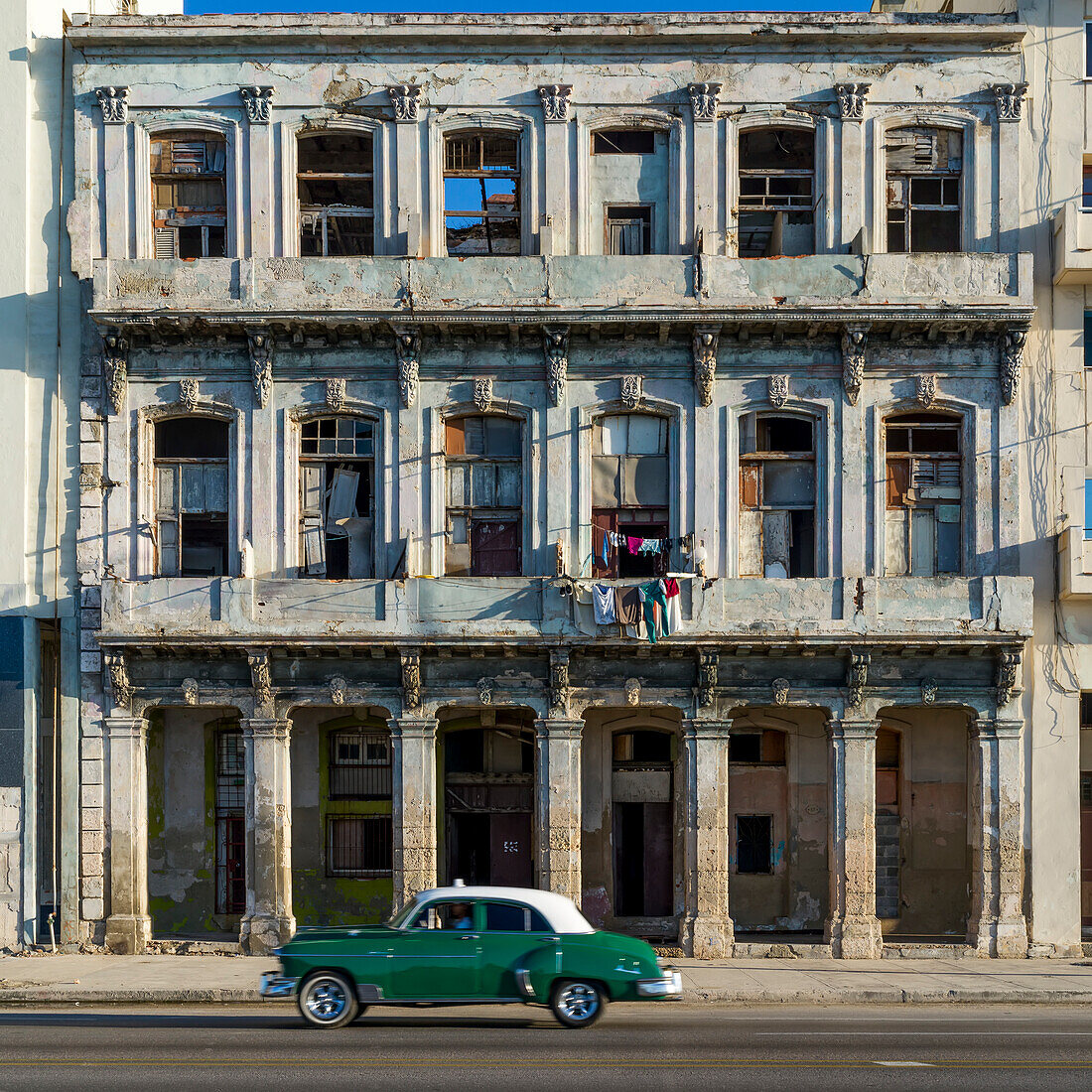 Ein altes Auto fährt an der verwitterten Fassade eines alten Gebäudes entlang einer Straße vorbei; Havanna, Kuba