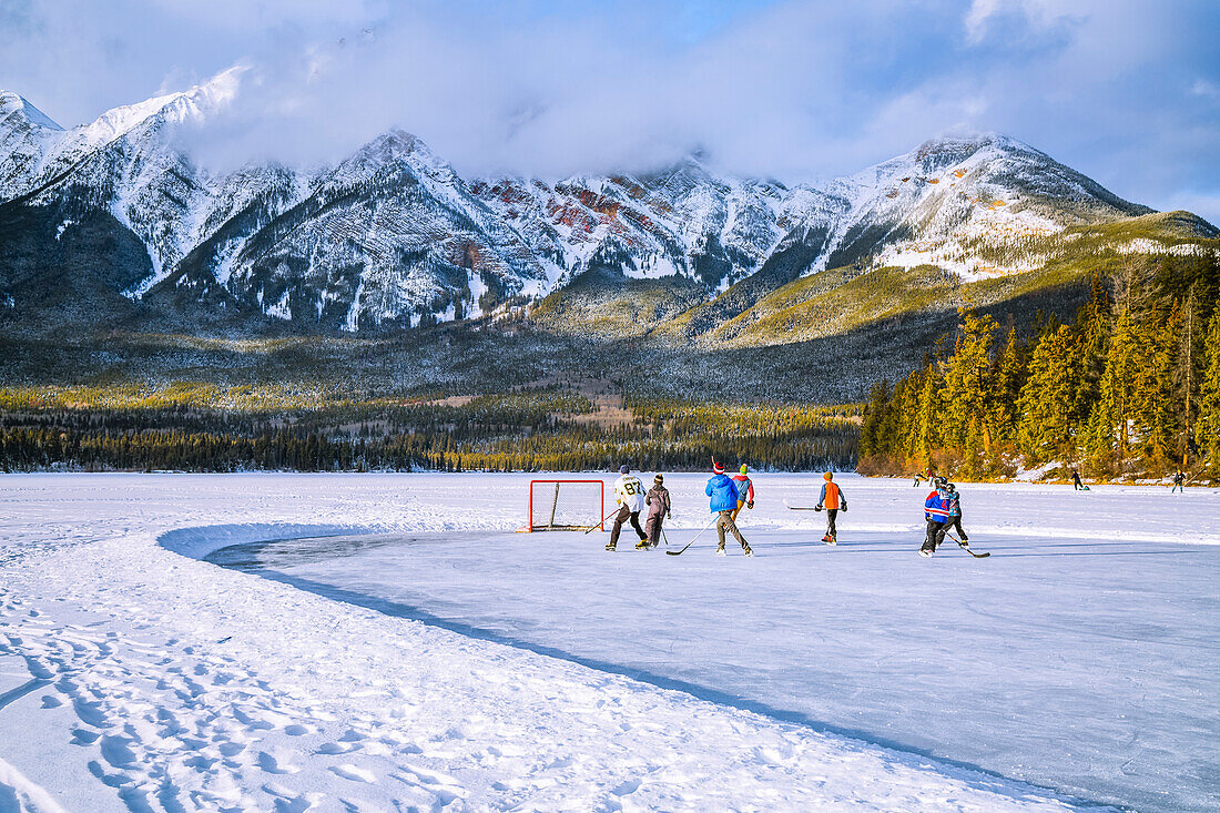 Gefrorener Pyramid Lake mit Kindern, die im Winter auf einer geräumten Eisbahn Eishockey spielen, Jasper National Park; Alberta, Kanada