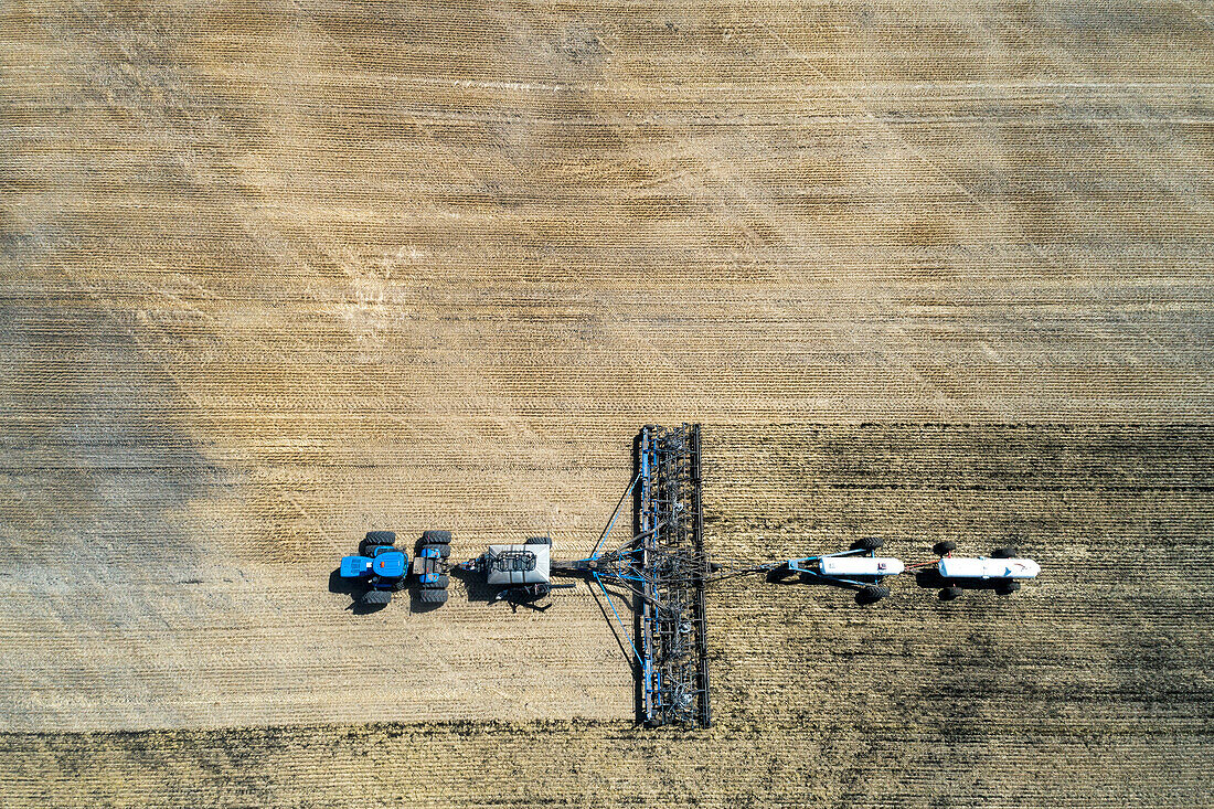 Luftaufnahme einer pneumatischen Sämaschine auf einem Feld mit weißen Ammoniaktanks in der Nähe von Beiseker; Alberta, Kanada