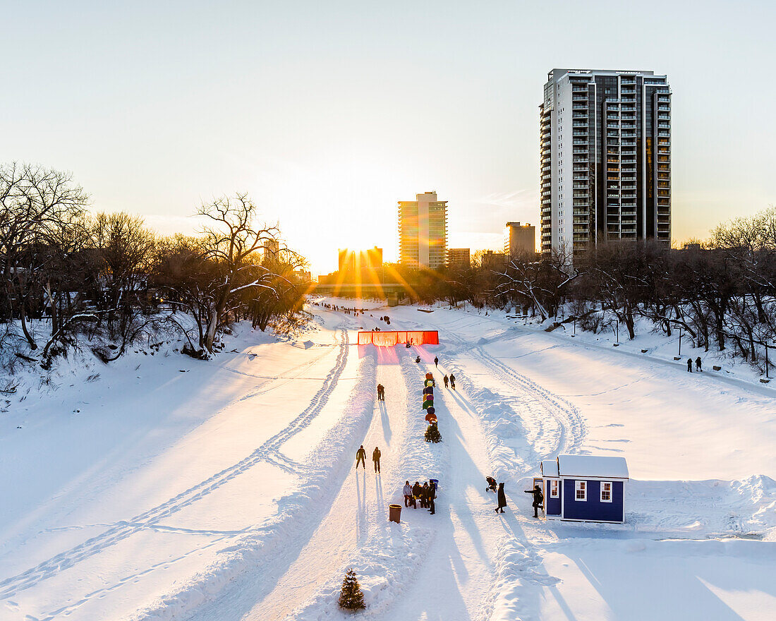 Ice skating at sunset on the Assiniboine River, part of the Red River Mutual Trail at The Forks; Winnipeg, Manitoba, Canada
