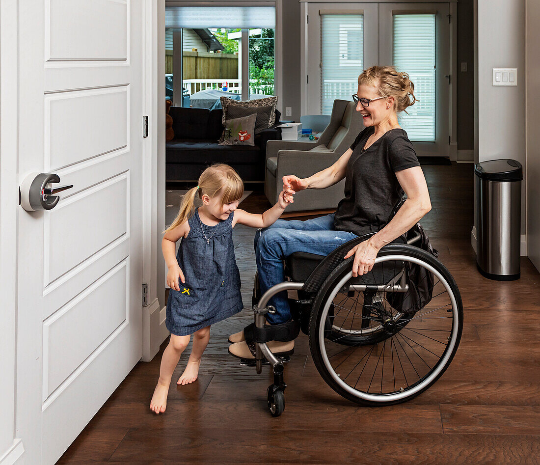 A paraplegic mother dancing with her daughter in the kitchen using her whellchair: Edmonton, Alberta, Canada