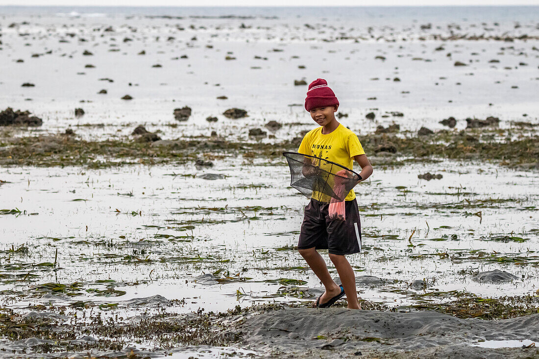 Junge, der bei Sonnenuntergang am Strand Muscheln sammelt; Lovina, Bali, Indonesien