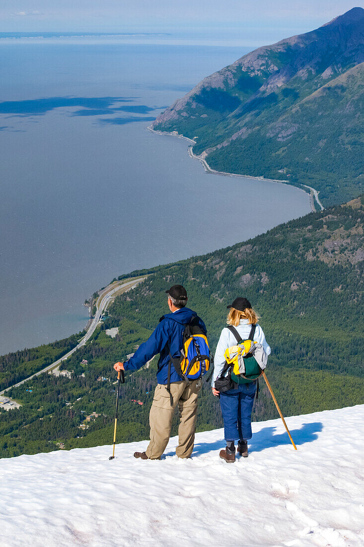 Hikers in the Chugach Mountains South of Anchorage, South-central Alaska. Summer. Couple is overlooking Turnagain Arm and the Seward Highway; Alaska, United States of America
