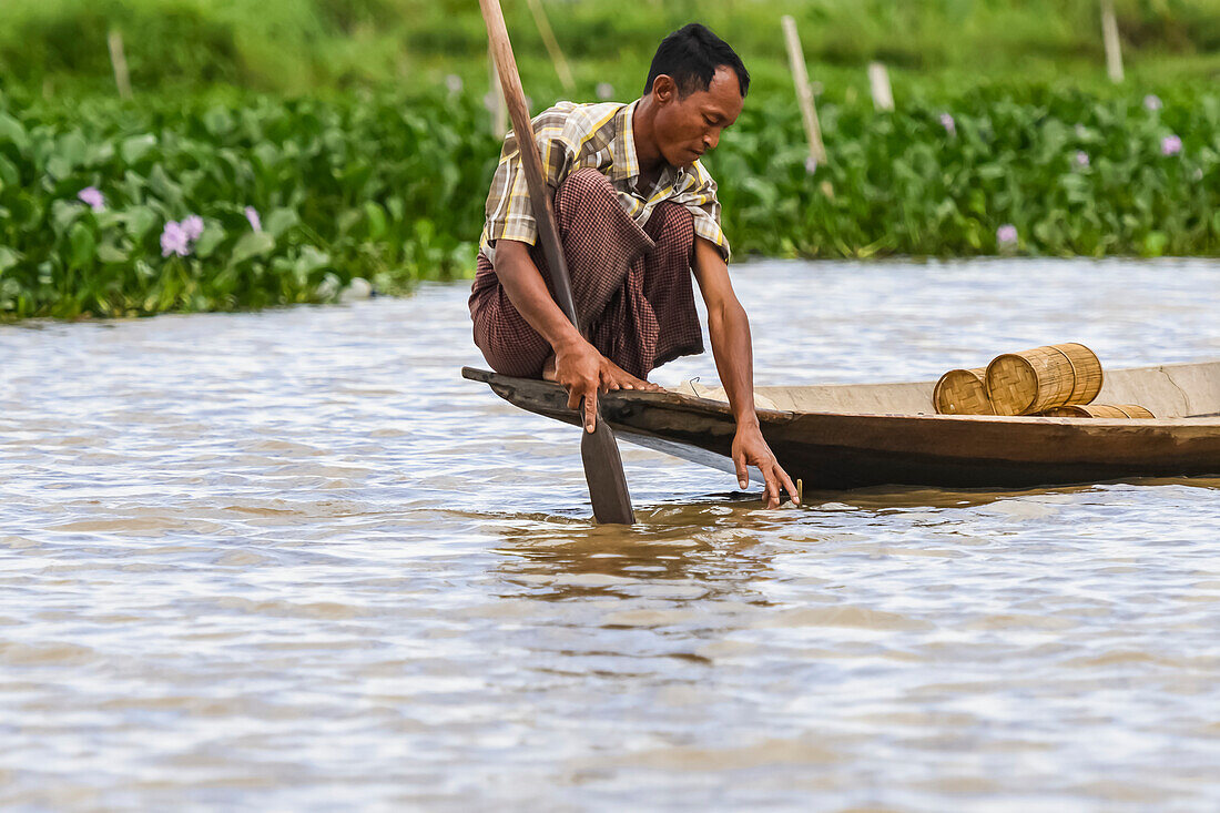 Man crouching on the edge of his boat with paddle; Yawngshwe, Shan State, Myanmar