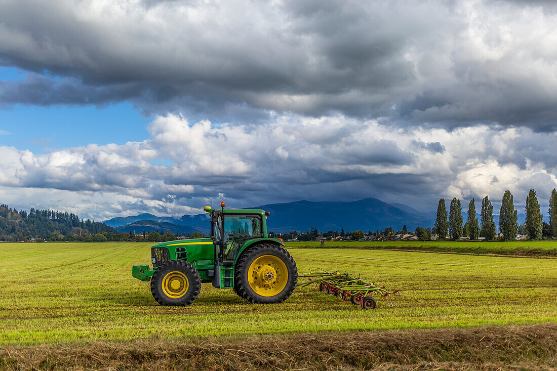 Traktor mit Anbaugerät auf Ackerland und Gewitterwolken über den Bergen; Washington, Vereinigte Staaten von Amerika