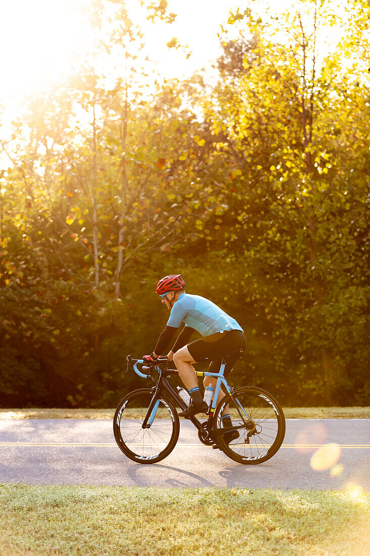 Radfahrer auf einer Straße mit hellem Sonnenlicht, das durch die Bäume dringt, in der Nähe der Trace Nachez Bridge; Franklin, Tennessee, Vereinigte Staaten von Amerika