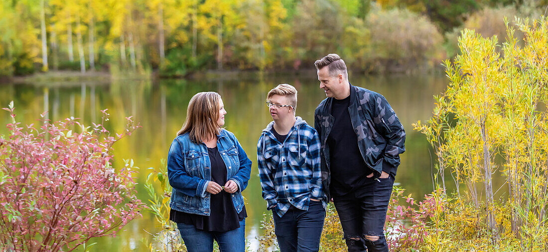 A young man with Down Syndrome walking with his father and mother while enjoying each other's company in a city park on a warm fall evening: Edmonton, Alberta, Canada
